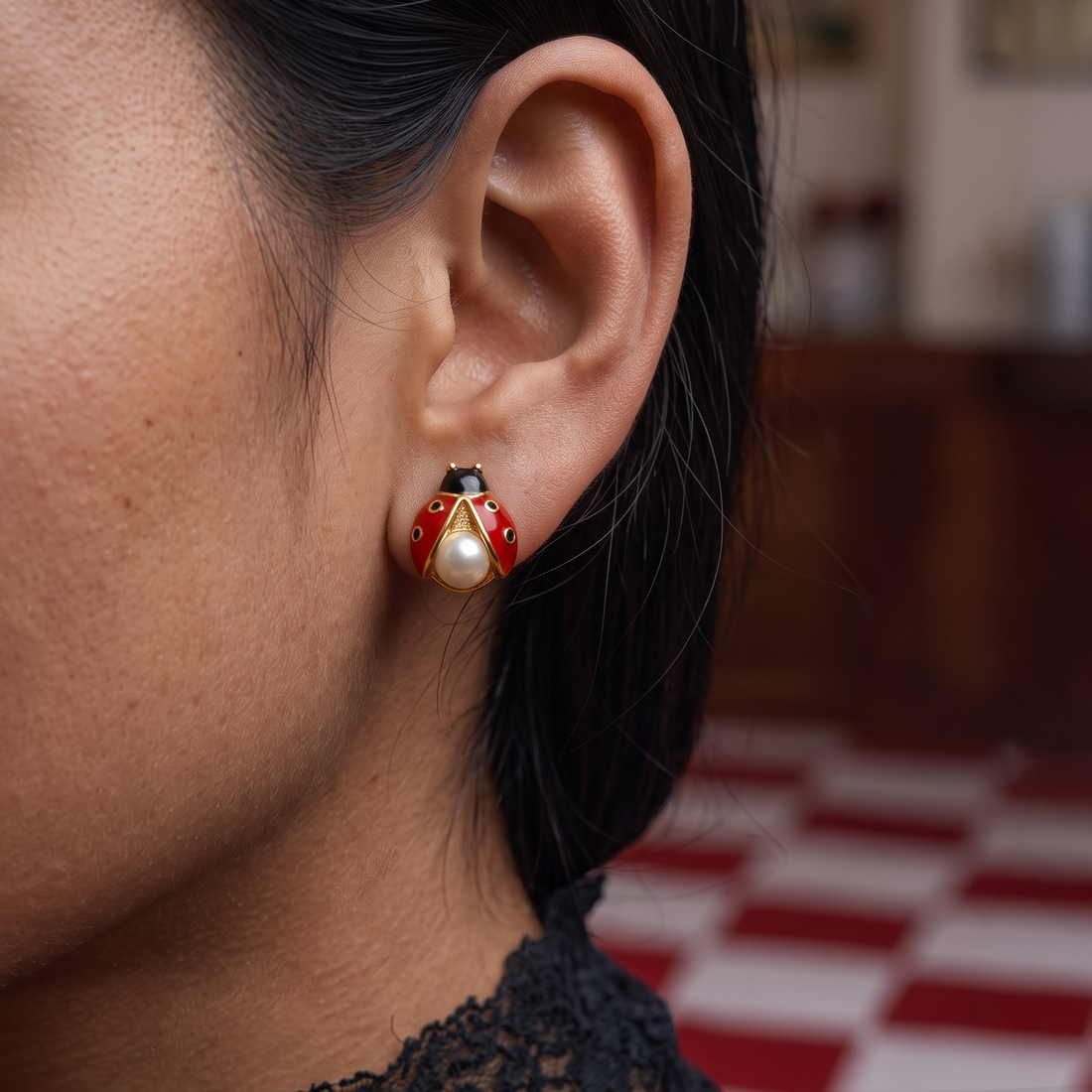 Ladybug Pearl stud earrings worn on the ear, red ladybug with black dots and a white pearl, checkered red backdrop