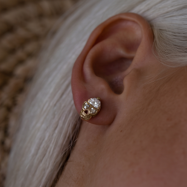 Crystal Skull stud earrings worn on the ear, gold skull with heart eyes and a large crystal on top