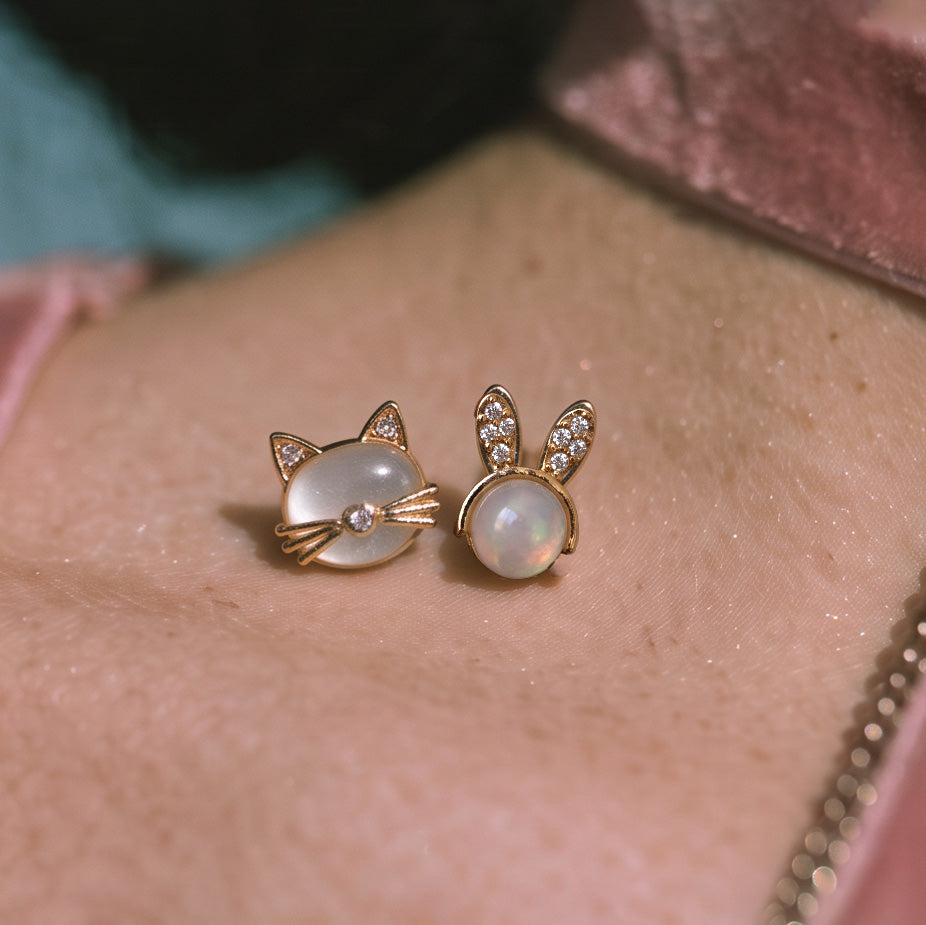 Mini Bunny stud earring paired with a cat-face stud, both gold with white centers, on skin