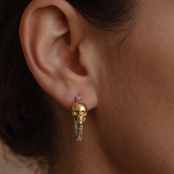 Skeleton Hoop earrings worn on the ear, a gold skull on a silver hoop, close-up against dark hair