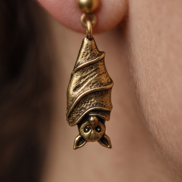 Sleeping Bat drop earrings, close-up of a gold bat with folded wings hanging from the ear