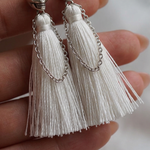 Skull Fringe Drop earrings close-up, two white tassels hanging below silver skulls, held in a hand