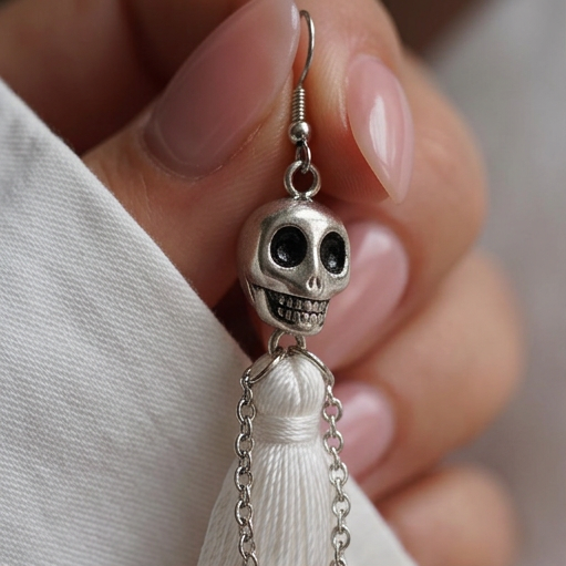 Skull Fringe Drop earrings, a silver skull on an ear wire held between fingers over a white sleeve