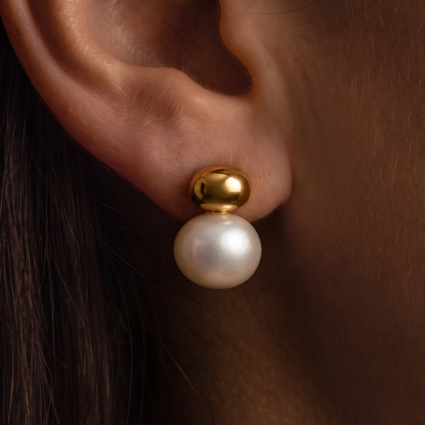 Gold Cap Pearl earrings worn on the ear, white pearl under a shiny gold dome, dark hair